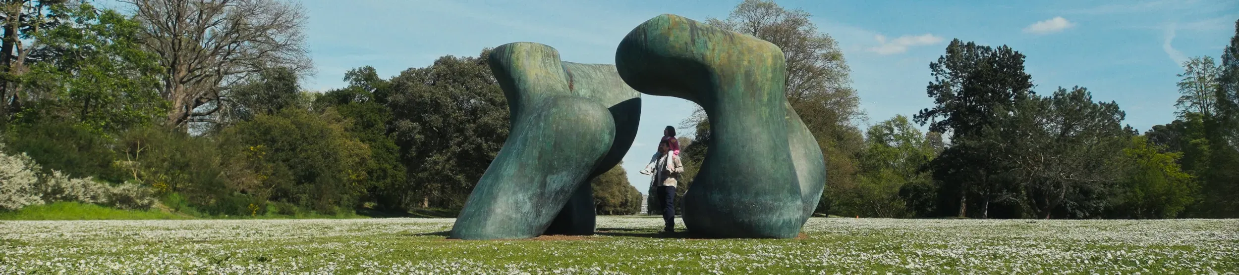 A man is walking through the sculpture Large Two Forms by Henry Moore with a young girl on his shoulders, who is looking up in awe