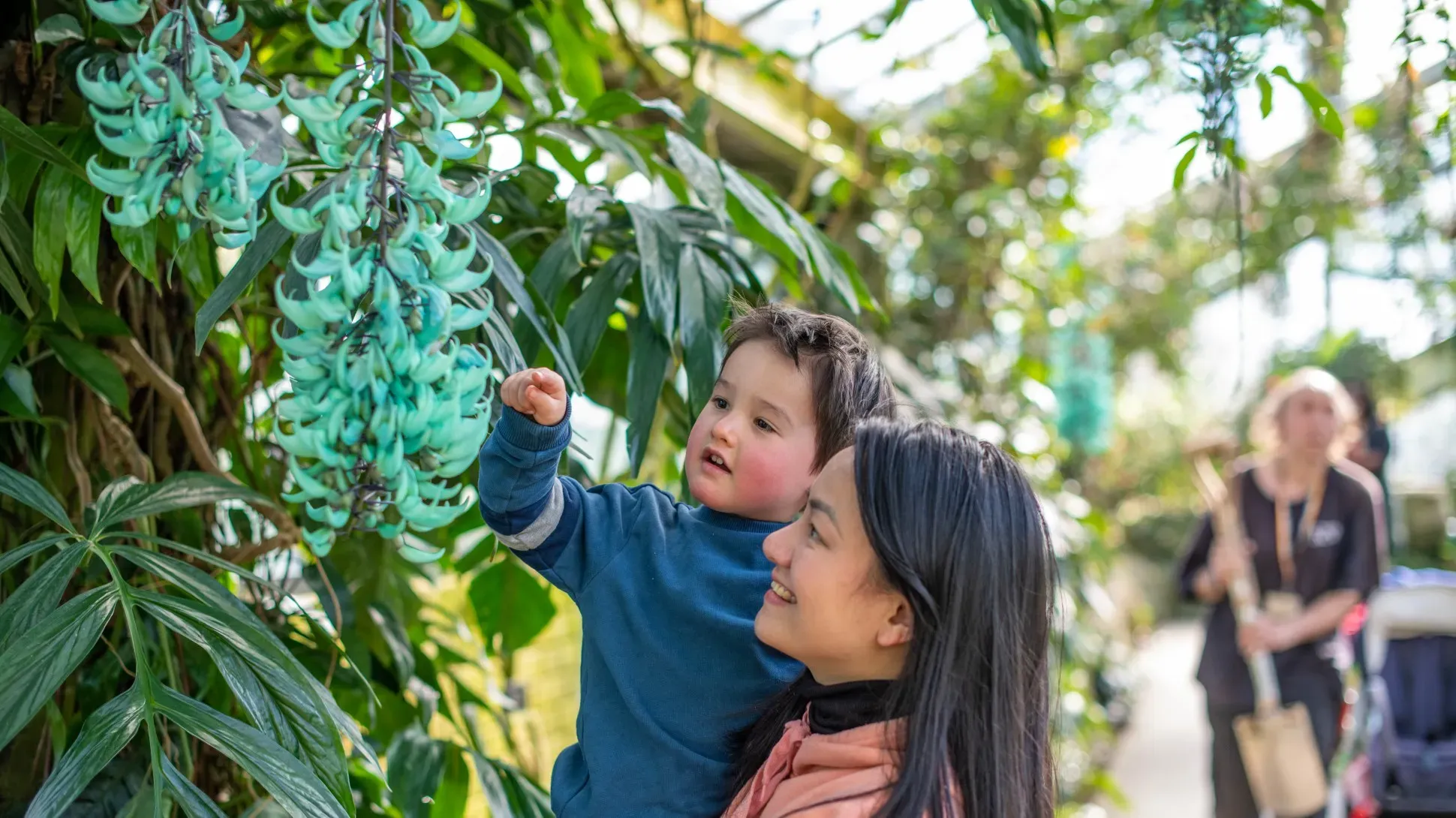 A woman holding a young child who is investigating a vibrant blue green flower