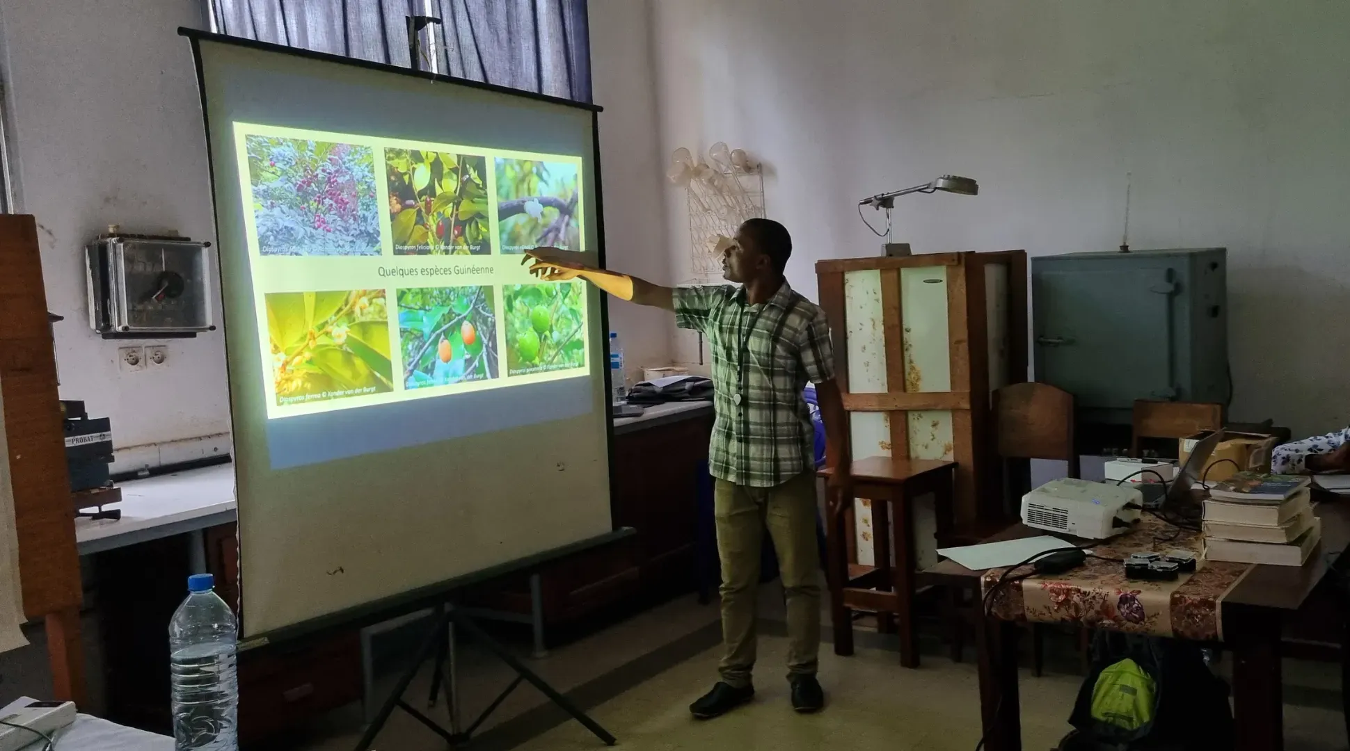 Faya Julien Simbiano standing in front of a projector teaching plant identification skills