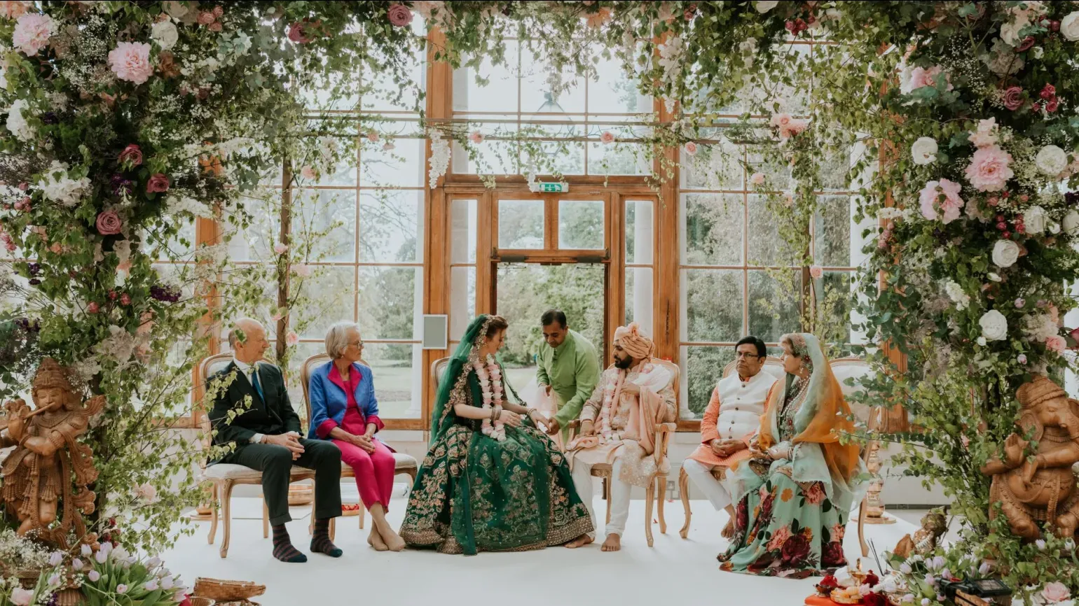 A wedding party sits under a floral archway in the nash conservatory