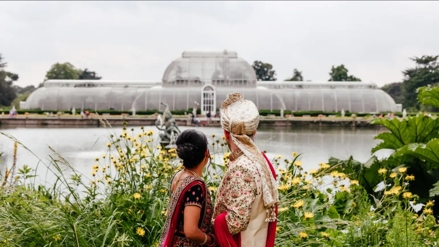 A wedding couple stand in front of the palm house at kew gardens