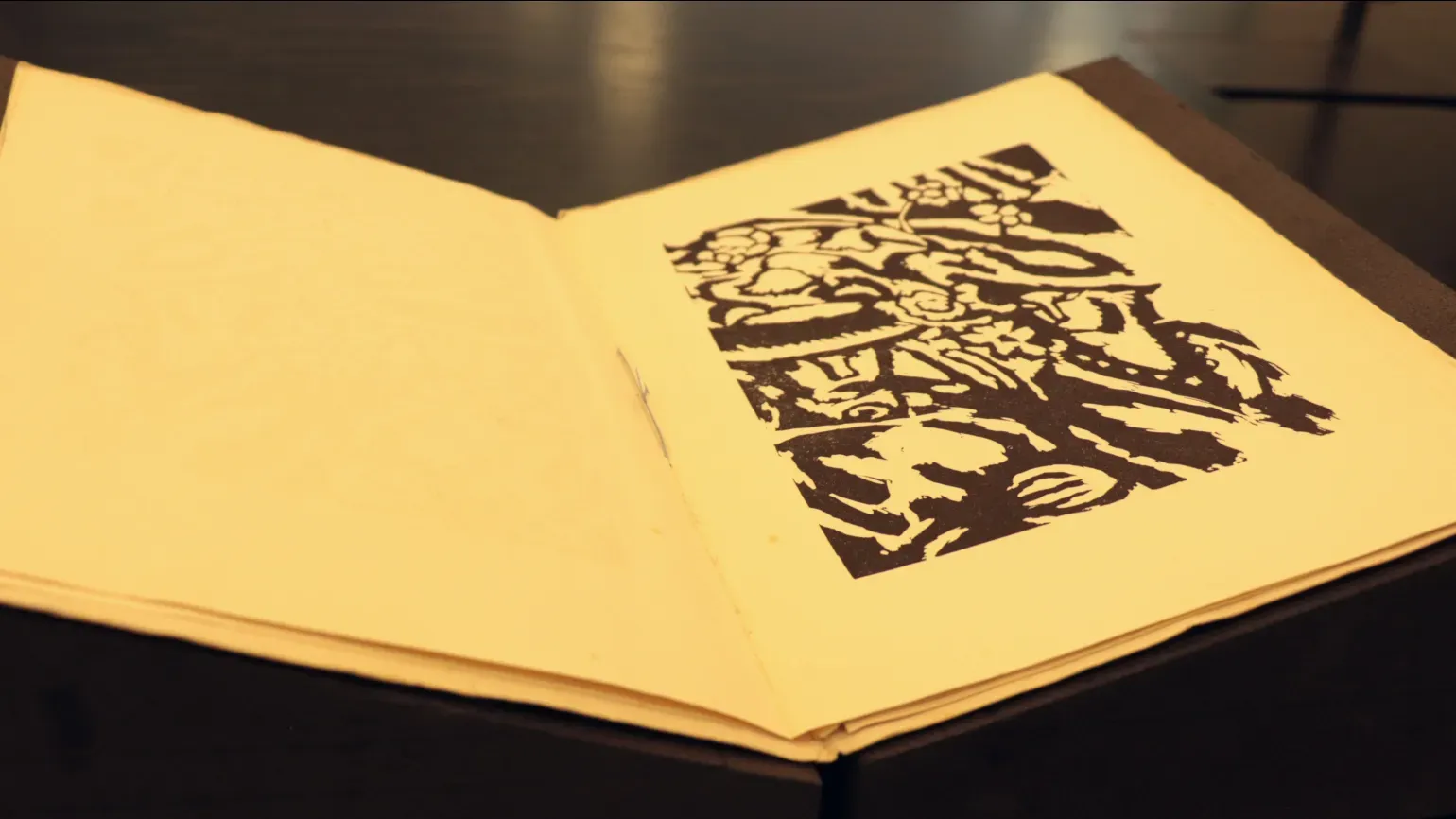 An old open book lies open displaying a stylised black and white woodcut of a man and woman wearing hats in a garden