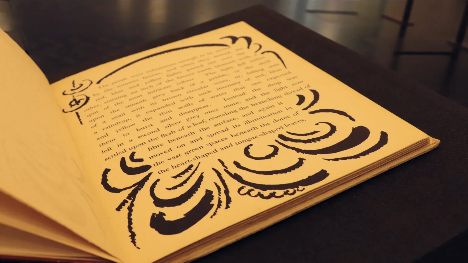 Open book on black background with black ink curved decorative markings around the text