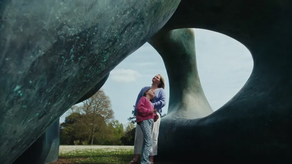 A woman and a young girl walking in between two sculptures, looking up at the parts over their heads in wonder.