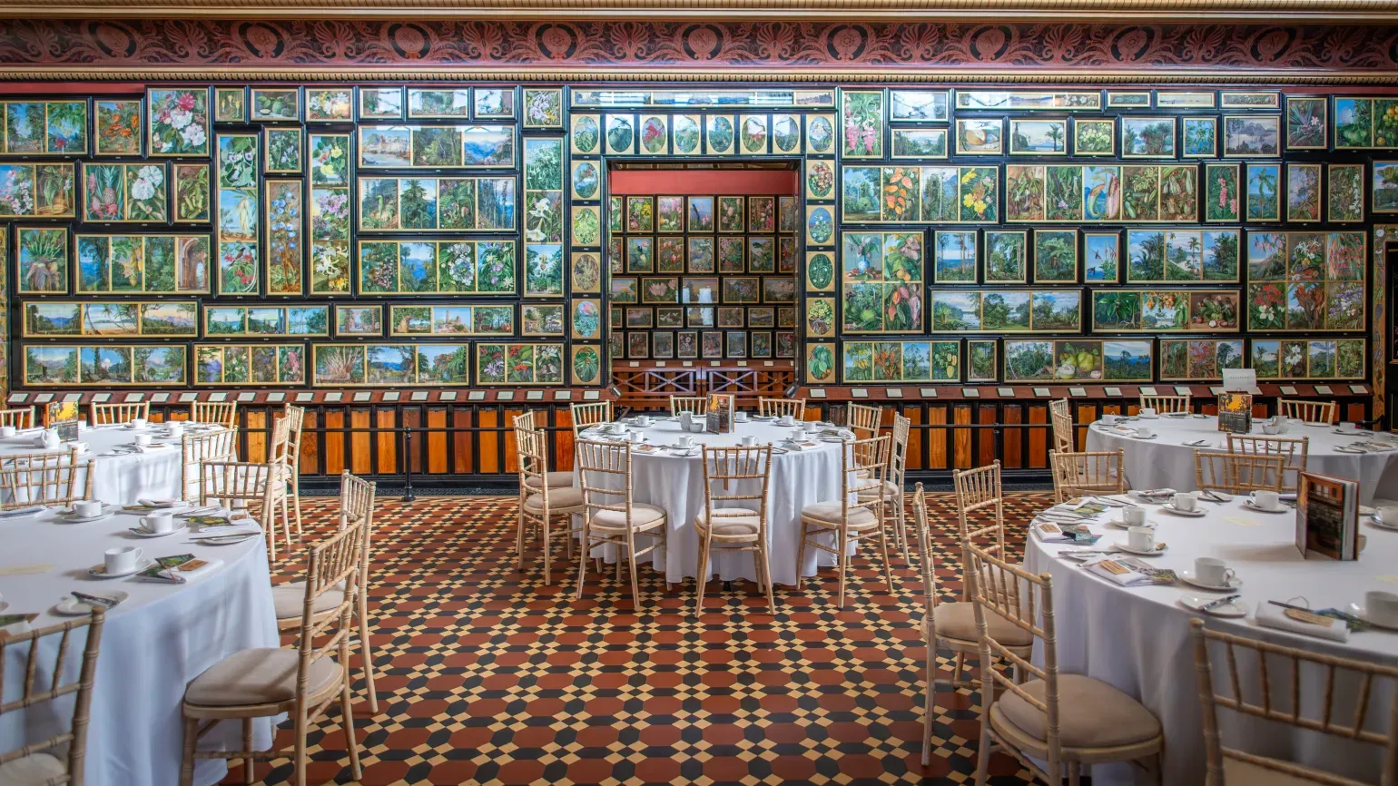 Formal tables and chairs inside a gallery lined with botanical paintings
