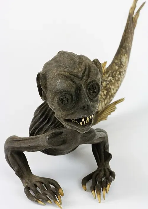 A small taxidermy-like figure combining a monkey-like head and torso with a fish tail, posed on all fours against a plain background.