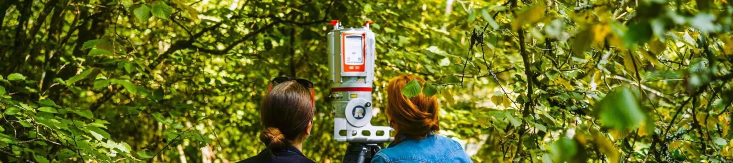 Two scientists stand in a woodland with a LiDAR scanner
