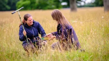 Two scientists sit in a meadow, holding a soil corer
