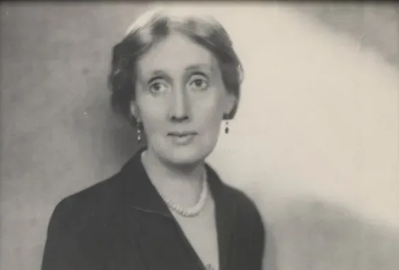Black and white photo of Virginia Woolf taken between 1930 and 1941. She is middle aged, wearing a low cut black dress and a pearl necklace
