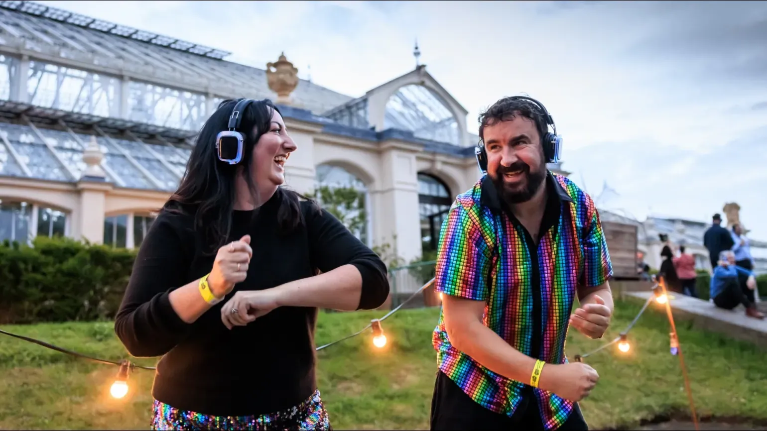 Two people with headphones dancing outside the Temperate House at Kew Gardens Silent Disco