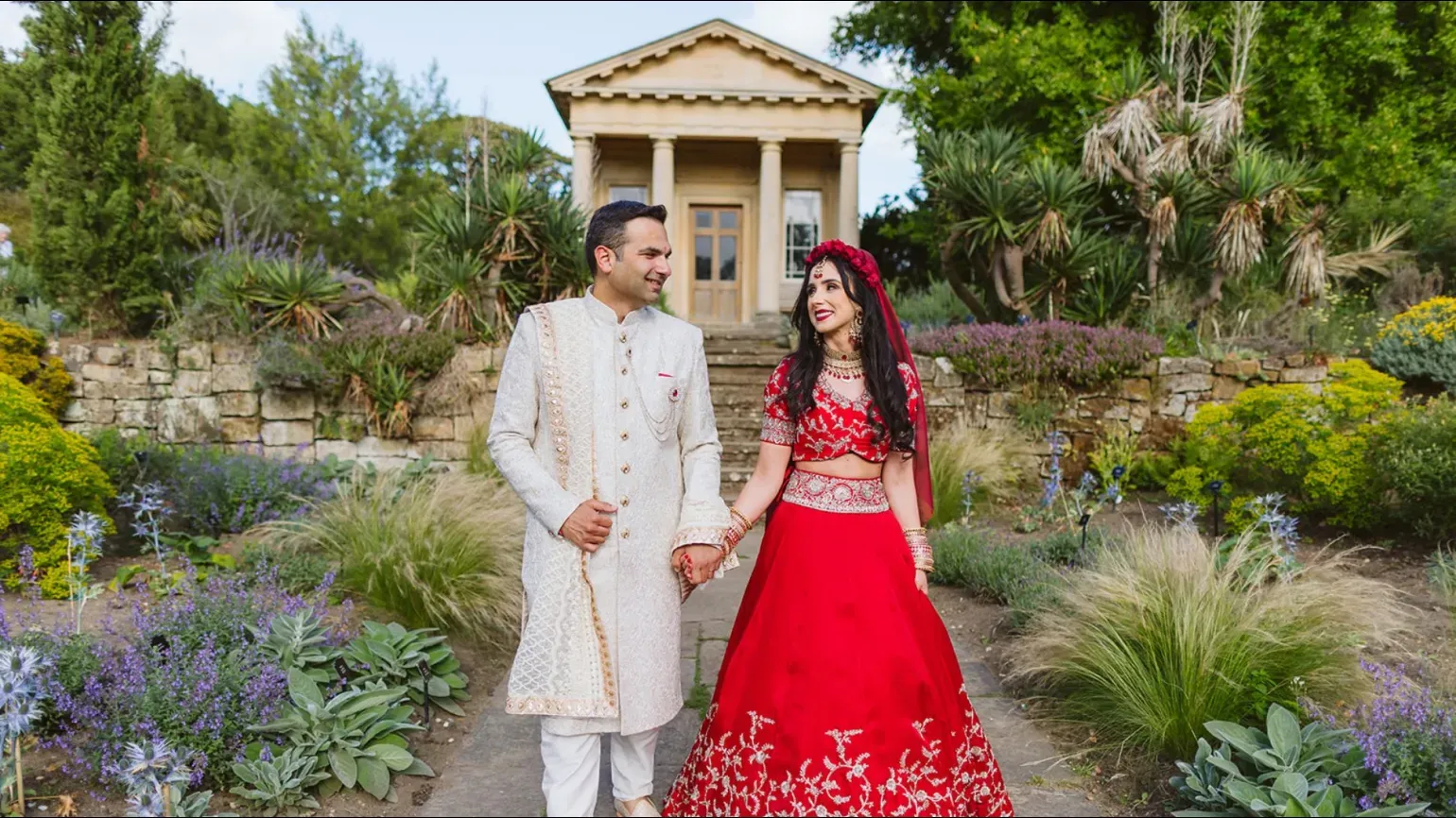 A south Asian wedding with bride in a colourful dress under a floral arch
