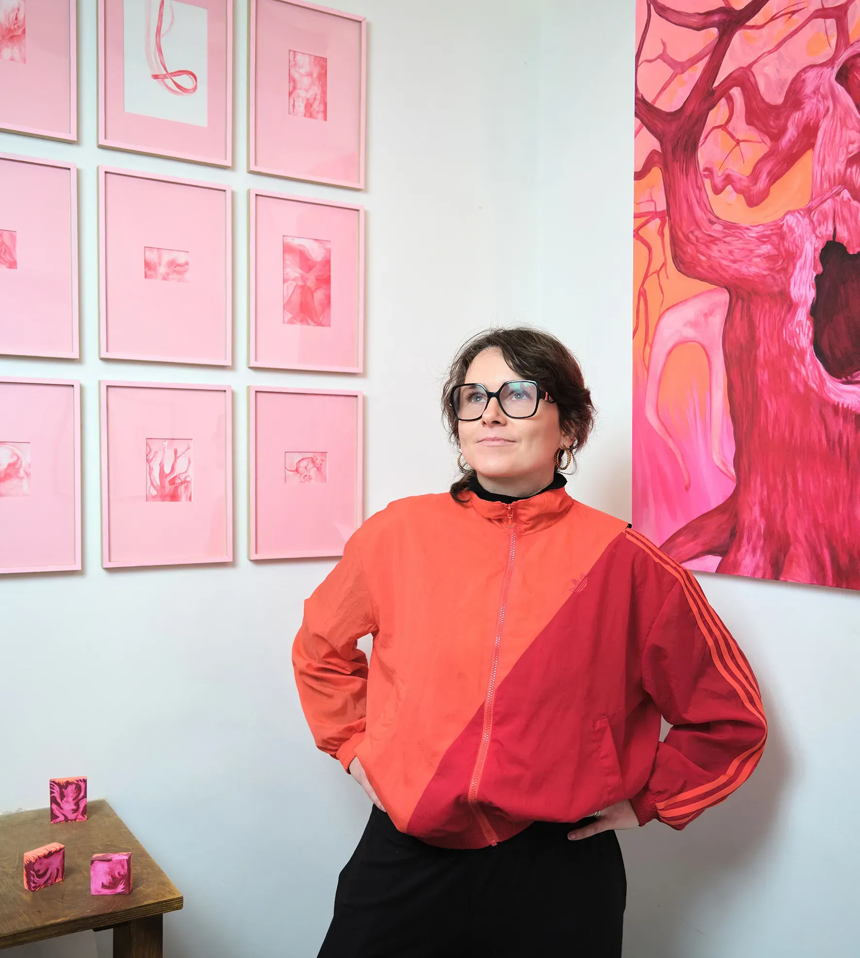 Woman in a red jacket wearing black glasses, standing in front of a wall of framed illustrative art.