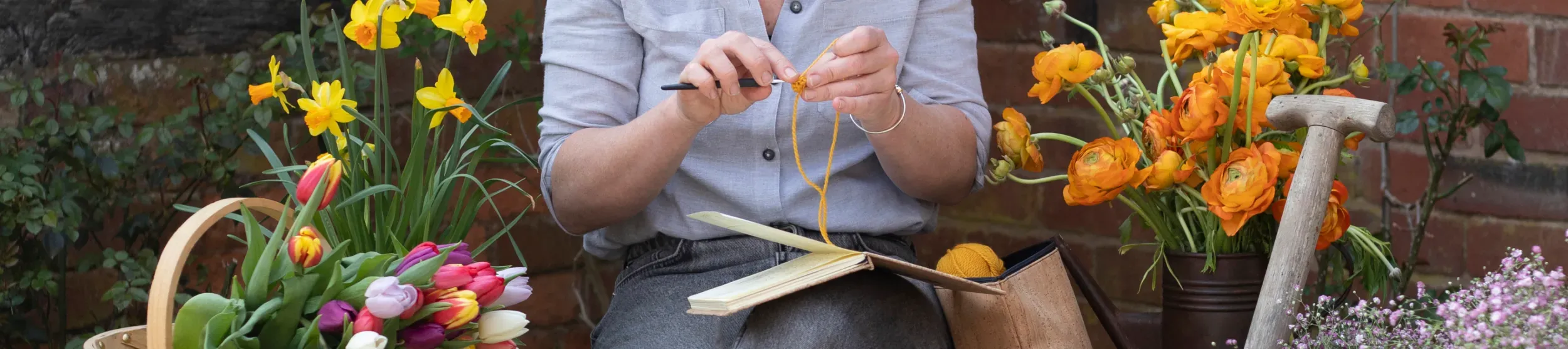 A person uses crochet hooks while sitting next to colourful flours