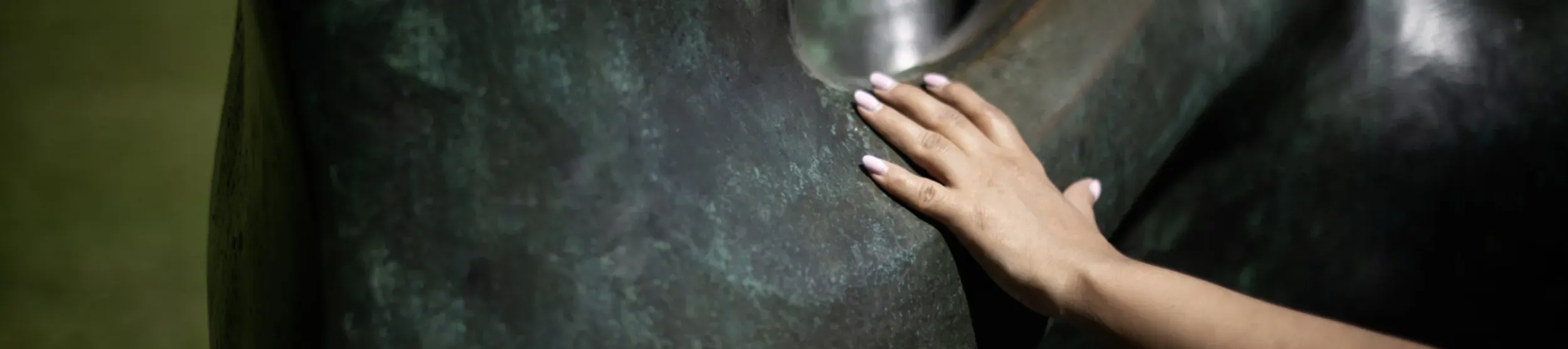 A close-up of a hand touching the bronze sculpture by Henry Moore, Reclining Mother and Child