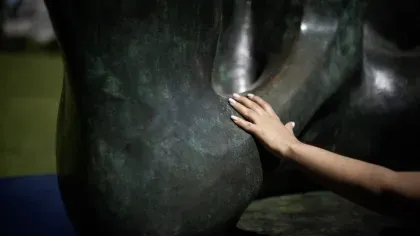 A close-up of a hand touching Henry Moore's sculpture Reclining Woman and Child, as part of the accessible touch tour offering
