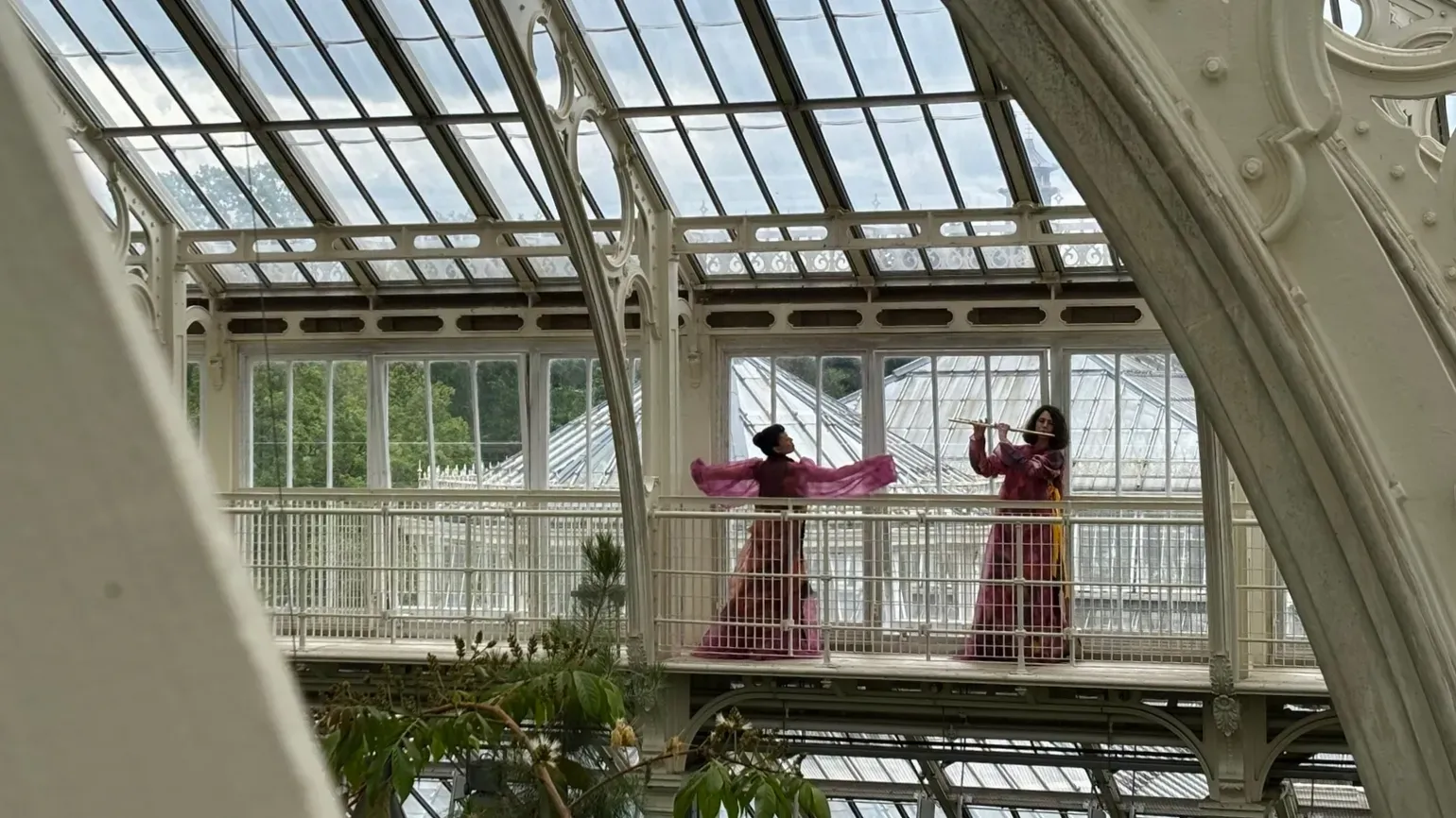 Two women, performing on the balcony in the Temperate House. They are both wearing bright pink dresses.