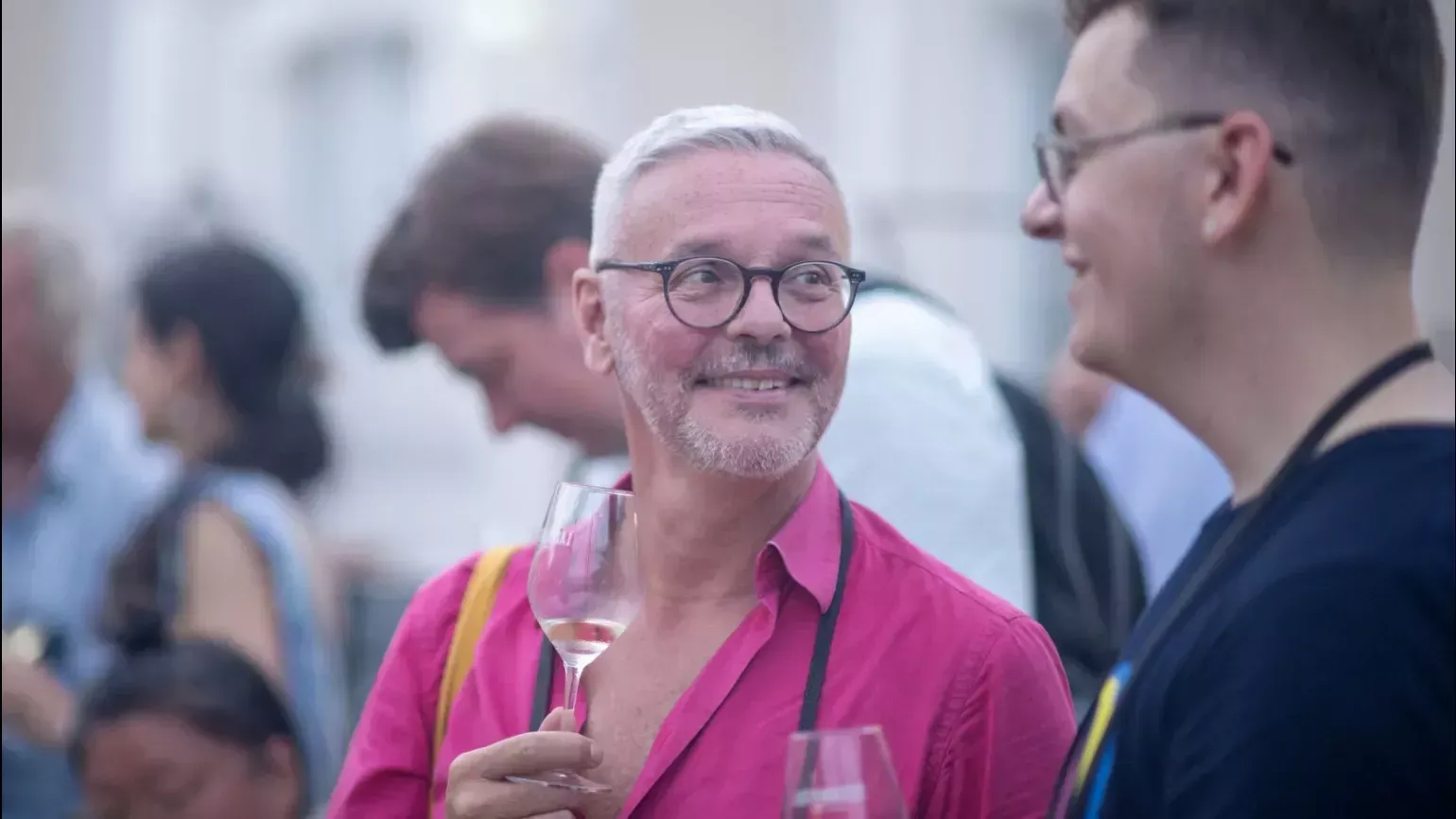 A man smiles and holds a glass of wine